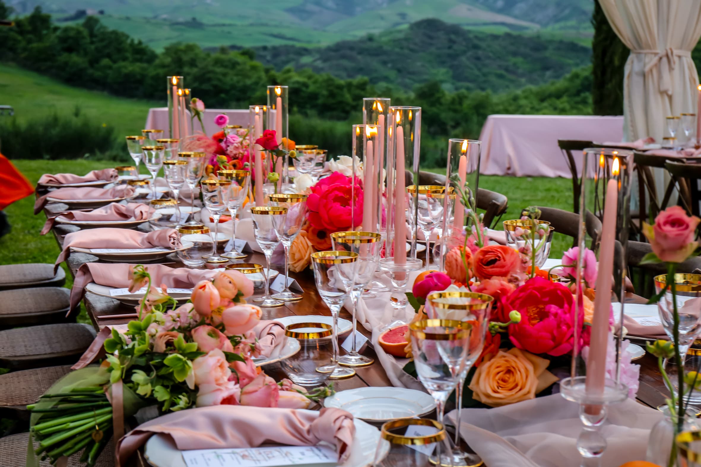 Tavola elegante con allestimento floreale e colline toscane al tramonto